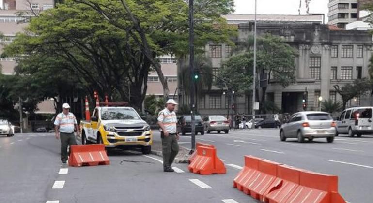 Dois agentes da BHTrans em avenida na Praça da Liberdade. Ao fundo há prédios e árvores