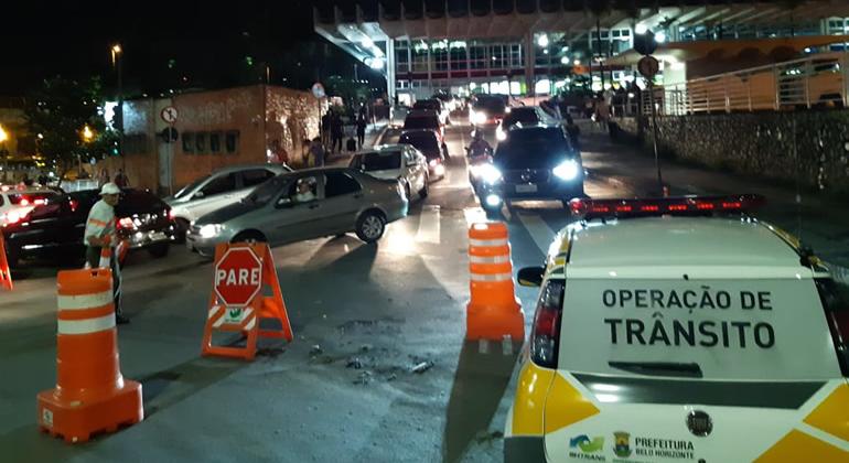 Fachada da Rodoviária, à noite, ao fundo, com carros da BHTrans fazendo operação de trânsito à frente. 