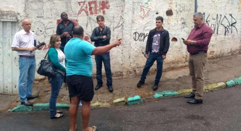 Sete pessoas na esquina de uma rua, durante o dia. 