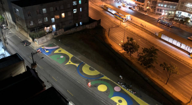 A intervenção, feita pela BHTrans, inclui uma nova pintura, plantas, guarda-sóis, bancos e outros elementos. Foto: Divulgação PBH Imagem aérea de rua pintada com círculos coloridos nas cores azul, amarelo, verde e rosa.