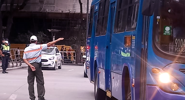 Transporte Coletivo tem alterações em função de obra realizada pela Prefeitura no bairro Sagrada Família, a partir de quinta, dia 30/5. Foto: Divulgação PBH Agente de trânsito coordena fluxo de carros, ao lado, ônibus passa.
