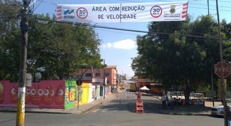 Rua semi-interditada com sinalização da BHTrans e um cartaz com os dizeres: "30 km. Área com redução de velocidade". 