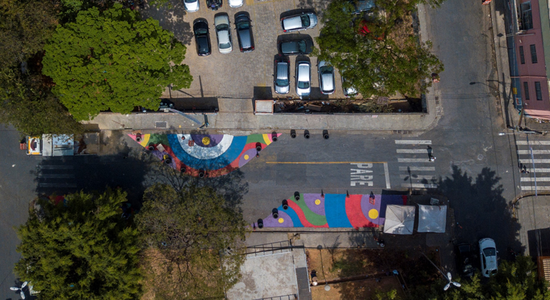 BHTrans está realizando uma série de atividades no Mês da Mobilidade Urbana, entre os dias 18 e 25/9. Foto: Divulgação PBH Imagem aérea de uma rua com pinturas e um estacionamento de carros ao lado, durante o dia.
