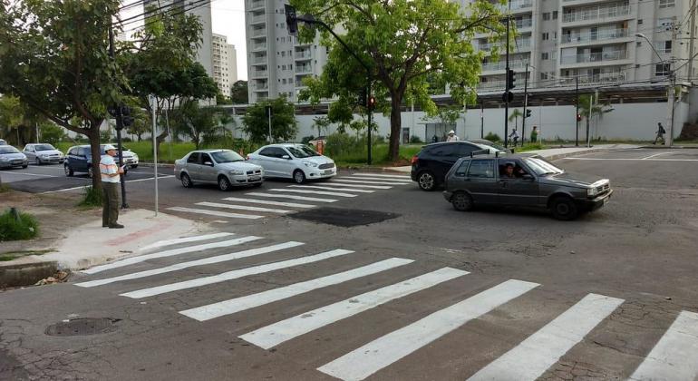 O trânsito melhorou depois da implantação da alça que liga as avenidas Tancredo Neves e a dos Engenheiros e foi criada a linha 5203. Foto: Gilvan Marçal/PBH Agente de trânsito na esquina e carros em trânsito na rua, no bairro Castelo, durante o dia.
