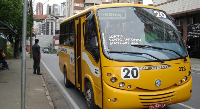 Transporte suplementar, representado por um ônibus menor de cor amarela, na rua, durante o dia.