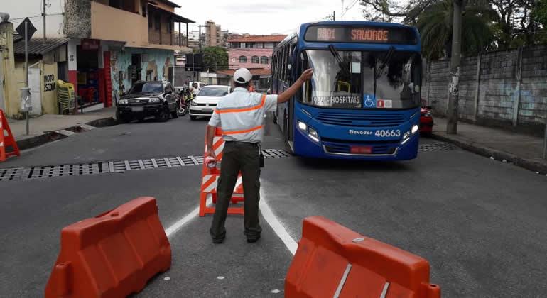 Fiscal de trânsito da BHTrans sinaliza para ônibus com o fronstispício escrito "Saudade", durante o dia. 