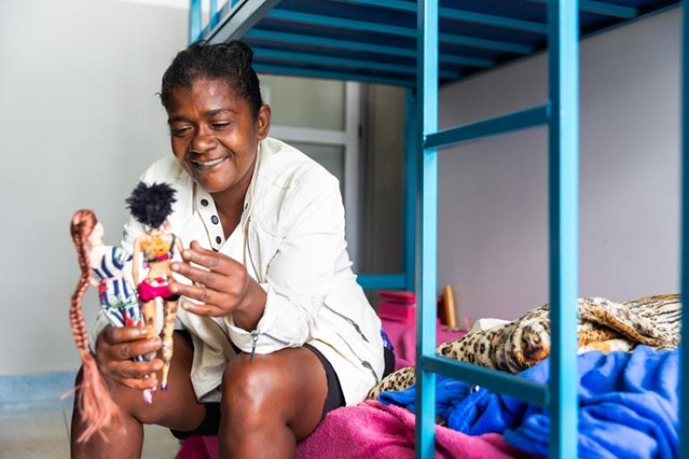 Prefeitura de BH passa a acolher famílias em situação de vulnerabilidade em novas unidades no Taquaril Mulher segura bonecas em um quarto da unidade de acolhimento do Taquaril.