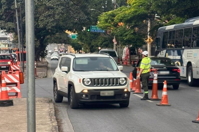 A imagem mostra Agentes da BHTrans sinalizando e orientando o trânsito na região do Expominas. Há um carro branco parado ao lado de uma fiscal da BHTrans.