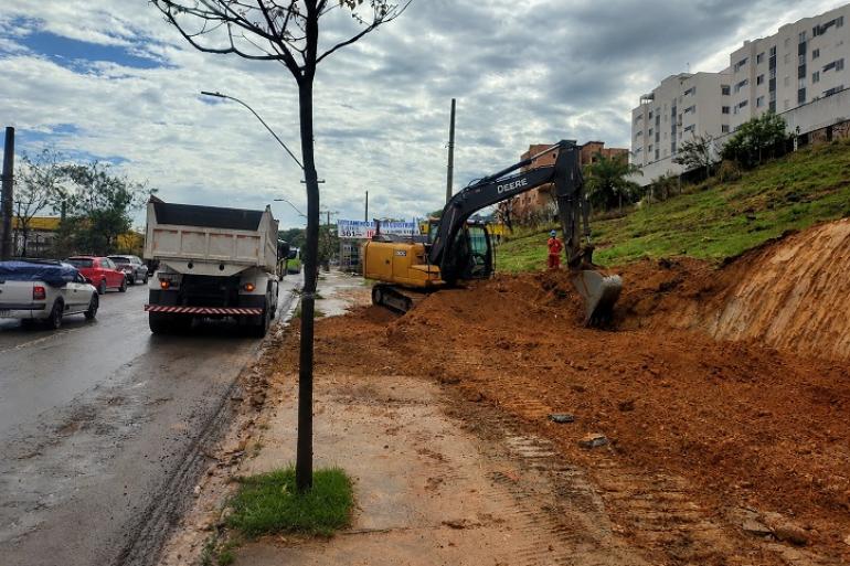 Avenida Cristiano Machado terá nova faixa de trânsito entre a Sebastião de Brito e a Waldomiro Lobo Imagem mostra uma avenida ao lado de um conjunto habitacional. Há também uma pequena árvore em primeiro plano na calçada. A foto também mostra um trtator escavando o terreno ao lado da avenida, um caminhao branco parado e alguns carros .