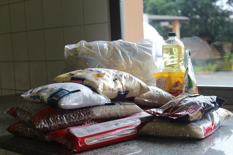 Parcerias fortalecem Banco de alimentos da PBH e beneficiam mais de 32 mil pessoas mensalmente Imagem mostra alimentos da cesta básica dispostos sobre uma mesa ao lado de uma janela.