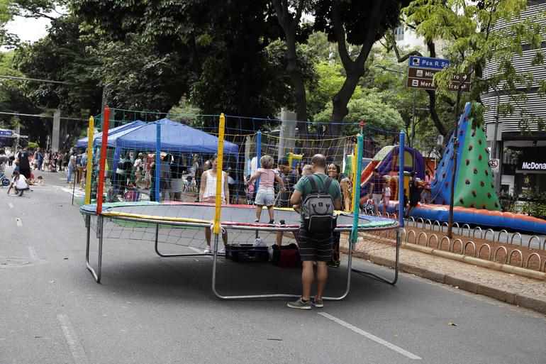 Criança pulando em uma cama elástica enquanto é vigiada pelos pais, na rua