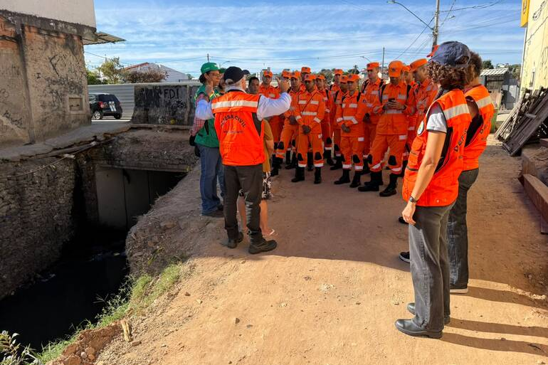 Grupo de agentes do Corpo de Bombeiros, reunidos com equipe da Defesa Civil, em uma rua de barro