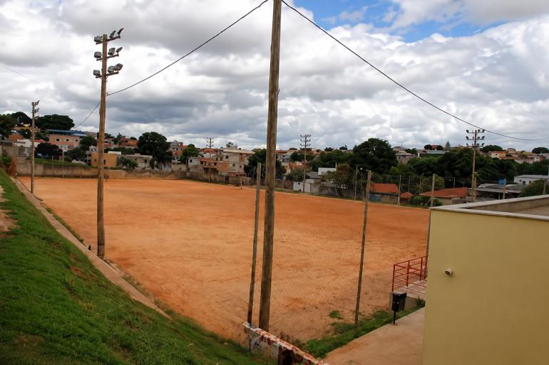 Campo de futebol do Providência, com piso de terra, poste de iluminação e parte gramada na arquibancada