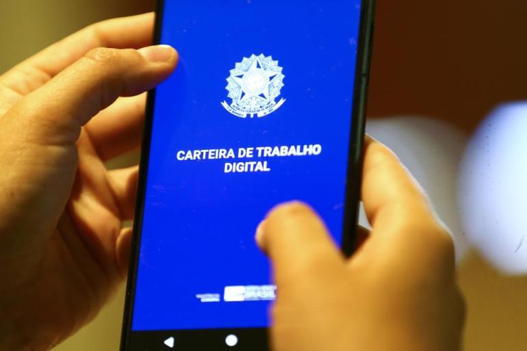 Imagem da Carteira de Trabalho Digital em telefone celular erguido por duas mãos