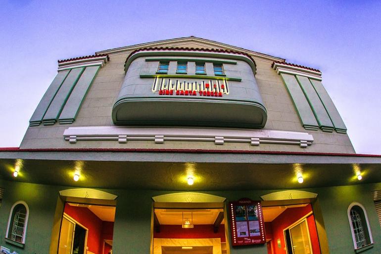 Cine Santa Tereza recebe mostra que revisita memórias do cinema de rua Fachada e do Cine Santa Tereza, vista de baixo para cima. O prédio verde destaca-se pelo letreiro luminoso vermelho "Cine Santa Tereza" numa varanda curva superior e por luzes a iluminar a entrada.