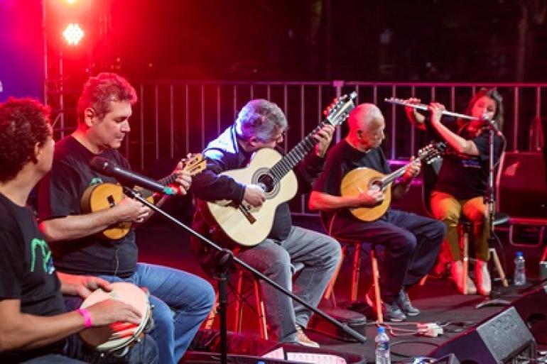 Clube de Choro de BH celebra 20 anos com show no Teatro Raul Belém Machado Cinco músicos do Clube do Choro sentados lado a lado em apresentaçãoa artística, tocando instrumentos variados: pandeiro, cavaquinho, violão, bandolim e flauta