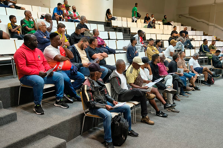 Em um auditório do Centro de Referência das Juventudes - CRJ, dezenas de representantes das equipes dos módulos A, B e C da Copa Centenário estão sentados em arquibancadas com cadeiras brancas. Alguns seguram documentos e acompanham atentamente as orientações do Congresso Técnico. O espaço é amplo, com piso acarpetado, paredes claras e iluminação interna.