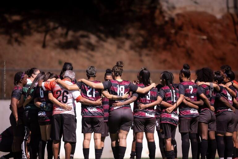 Copa Centenário terá 15 partidas programadas neste fim de semana Time de futebol feminino, usando uniforme preto e vermelho listrado, em um abraço coletivo junto ao técnico