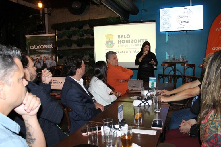 Fiscalização reforça diálogo e equilíbrio com setor de bares e restaurantes em encontro na Pampulha Imagem mostra a subsecretária de Fiscalização, Iara França discursando para uma plateia de empresárioscom a identidade visual da PBH ao fundo.
