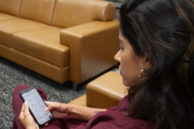 Em uma década, PBH amplia em mais de 500% serviços digitais, simplifica processos e melhora a jornada do cidadão Imagem mostra uma cidadã consultando o serviço da PBH pelo celular. Ao fundo há um sofá bege.