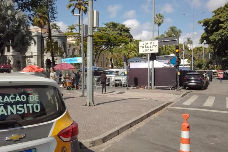 Operação de trânsito e transporte para o “Festival Mineiro da Cerveja” neste sábado (22), na Savassi Foto diurna de uma rua na região da Praça da Liberdade, em Belo Horizonte. Em primeiro plano à esquerda, aparece a traseira de uma viatura da BHTrans. À direita, na pista, há um cone de sinalização laranja e branco.