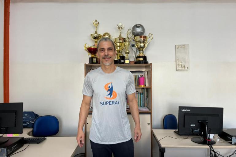 Programa Superar oferece 2,5 mil atendimentos por mês com atividades esportivas para pessoas com deficiência O professor Frederico Toledo, de cabelos grisalhos e barba curta, está em pé, no centro de uma sala, sorrindo para a câmera. Ele veste camiseta cinza com a logomarca e a palavra Superar em azul e laranja, e calça escura.