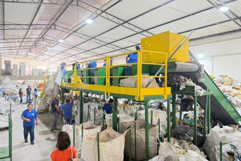 Catadores cooperados trabalham próximo à maquina e material reciclável em galpão entregue pela PBH