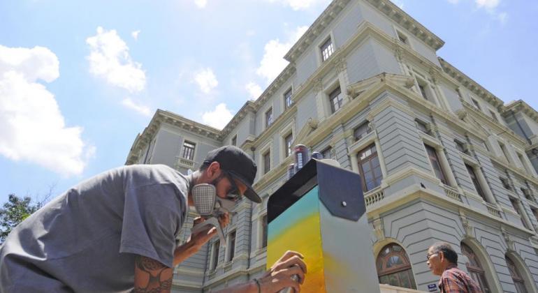 Artista grafita lixeira com prédio histórico da praça da liberdade ao fundo