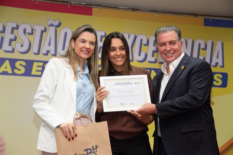 Foto da secretária de Educação, Natália Araújo, ao lado de gestora de escola e do prefeito Álvaro Damião em cerimônia pela melhoria do Ideb