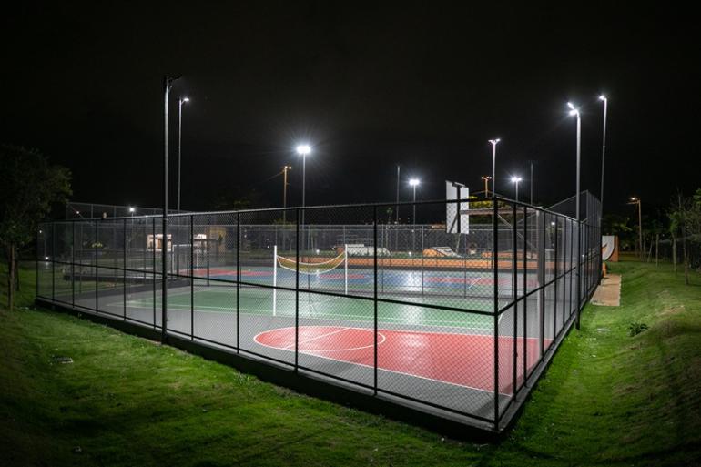 Ilumina BH reestrutura a iluminação de campos de futebol, quadras esportivas, pistas de skate e de caminhada por toda a cidade Quadra de esporte pintada de verde, vermelho e azul, cercada por tela, sem nenhuma pessoa, num ambiente noturno que ressalta a iluminação com postes.