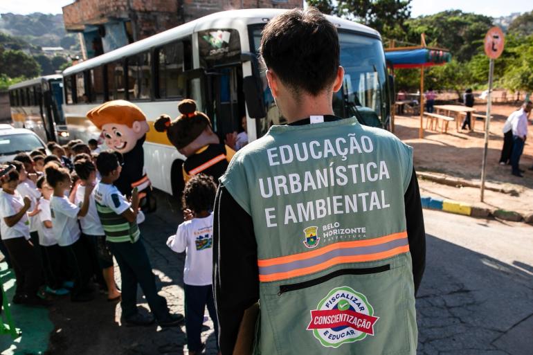 Estudantes participam de mutirão que recolheu cinco caminhões de lixo no Novo Aarão Reis Fiscal com colete com os dizeres "Educação Urbanística e Ambiental" observa crianças que chegam ao local do mutirão