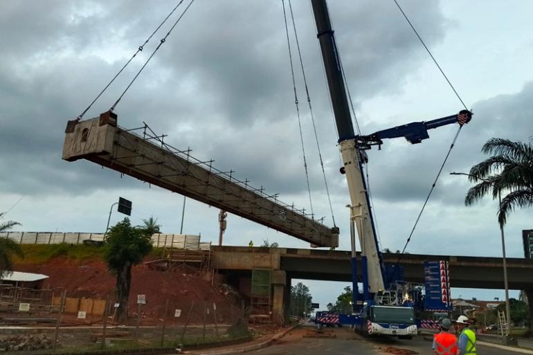 Imagem mostra uma estrutura de concreto sendo erguida por um guindaste, no viaduto do bairro Belvedere, próximo ao BH Shopping. Sob céu nublado, alguns operários acompanham o içamento da viga.