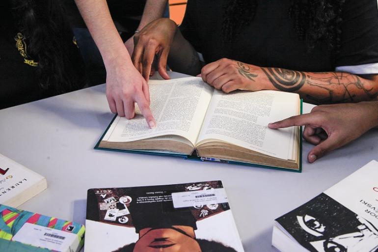 Alunos do 9º ano da rede municipal conquistam bronze na 18ª Olimpíada Nacional de História Mãos de alunos apontam para livro de história que está aberto sobre a mesa ao lado de outras publicações .