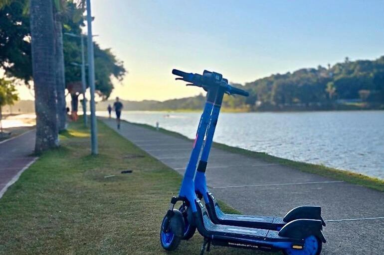 Patinetes elétricos chegam à Pampulha neste domingo (19) Patinete elétrico na cor azul, ao fundo, Lagoa da Pampulha e pôr-do-sol, enquanto pessoas correm e caminham na Orla da Lagoa da Pampulha