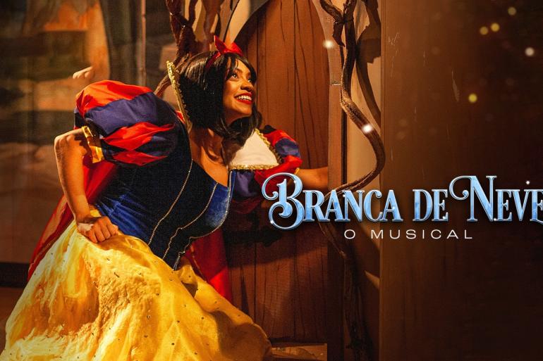 Atriz vestida como Branca de Neve segura a saia rodada e amarela do seu vestido enquanto espreita por uma porta de madeira. A roupa conta com corpete azul, mangas bufantes em azul e vermelho com acabamento amarelo, capa vermelha sobre as costas e um laço vermelho no cabelo. À direita, lê-se o texto "Branca de Neve, O Musical".