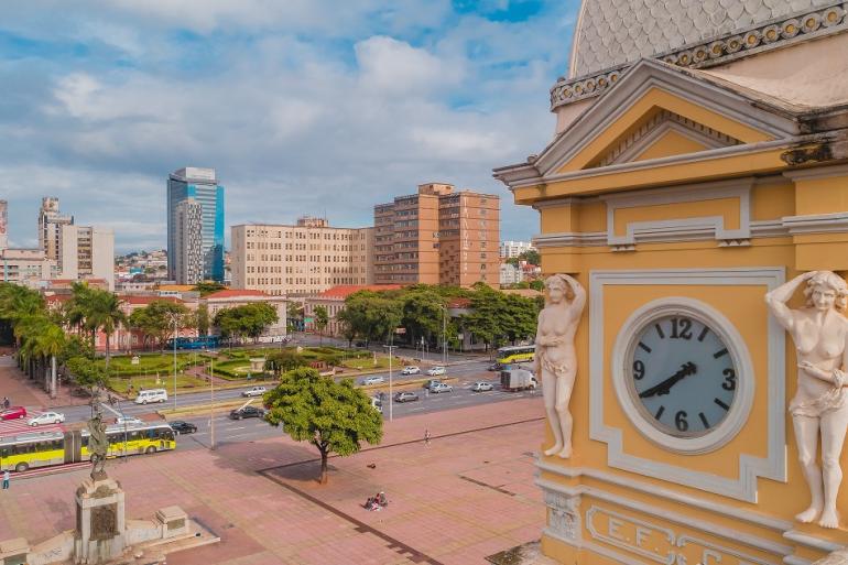 Vista aérea da Praça da Estação, em Belo Horizonte, com o relógio do Museu de Artes e Ofícios em primeiro plano. Ao centro, aparece o pátio da praça e, ao fundo, a Avenida dos Andradas.