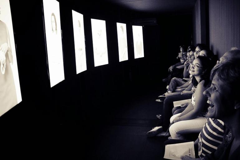 Exposição Sentidos do Nascer oferece experiência interativa gratuita sobre gestação, parto e nascimento A imagem em preto e branco, mostram a reação de um público durante uma exposição ou instalação audiovisual.
