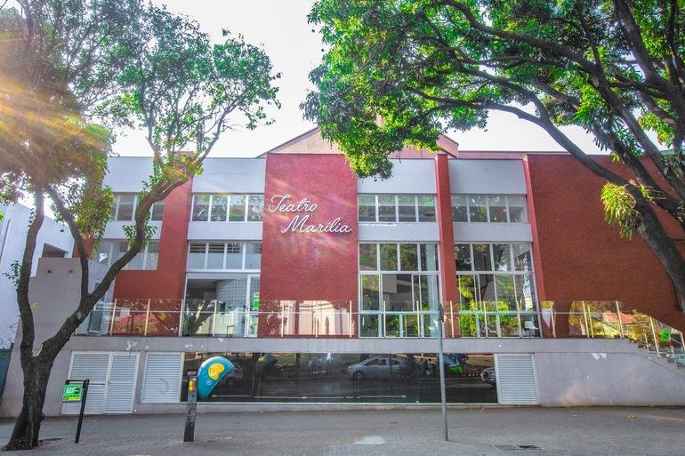 Fechada do Teatro Marília, em cores vermelhas e brancas, e rua com um orelhão de telefonia e lixeira com adesivo verde da SLU