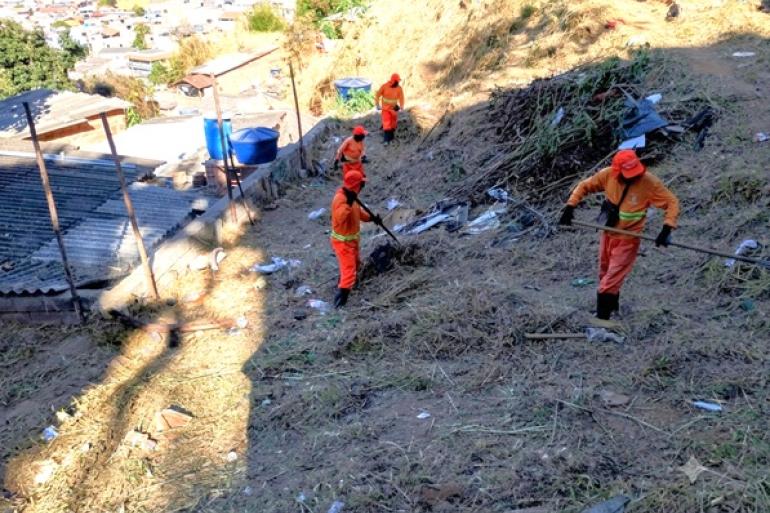 Funcionários da SLU, usando uniformes laranja e portando ferramentas, participam de mutirão de limpeza