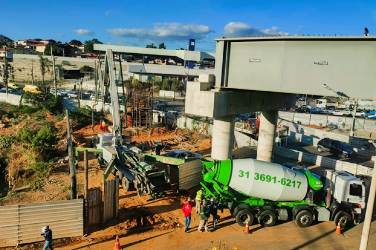 PBH inicia nova etapa das obras do viaduto na Cristiano Machado com Sebastião de Brito Imagem mostra obra na interseção das avenidas Sebastião de Brito e Cristiano Machado, em Belo Horizonte. Em primeiro plano, há trabalhadores e máquinas atuando em uma área de terra escavada, sob uma estrutura elevada de concreto. Um caminhão betoneira verde está estacionado no local, ao lado de equipamentos e materiais de construção. Ao fundo, aparecem a pista da Avenida Cristiano Machado, com veículos em circulação, além de imóveis comerciais e residenciais. O céu está azul e parcialmente nublado.
