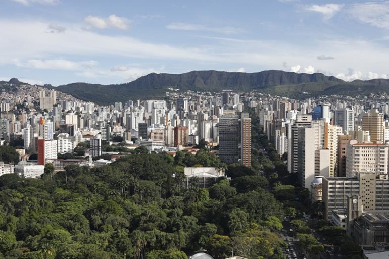 Vista panorâmica da cidade de Belo Horizonte, com imagens de árvores, vários prédios e a Serra do Curral ao fundo