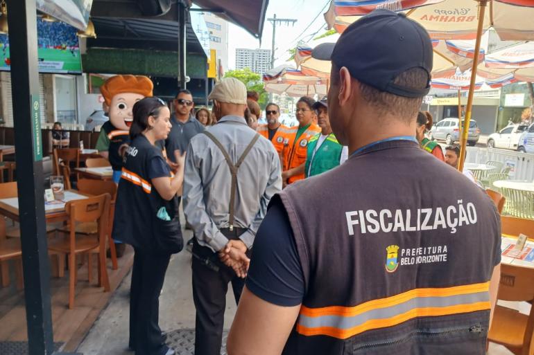 Prefeitura de BH orienta comerciantes da Rua Alberto Cintra sobre descarte de lixo para evitar alagamentos Servidores da Fiscalização, usando coletes de trabalho, conversam com comerciantes na Rua Alberto Cintra em frente a um estabelecimento comercial.