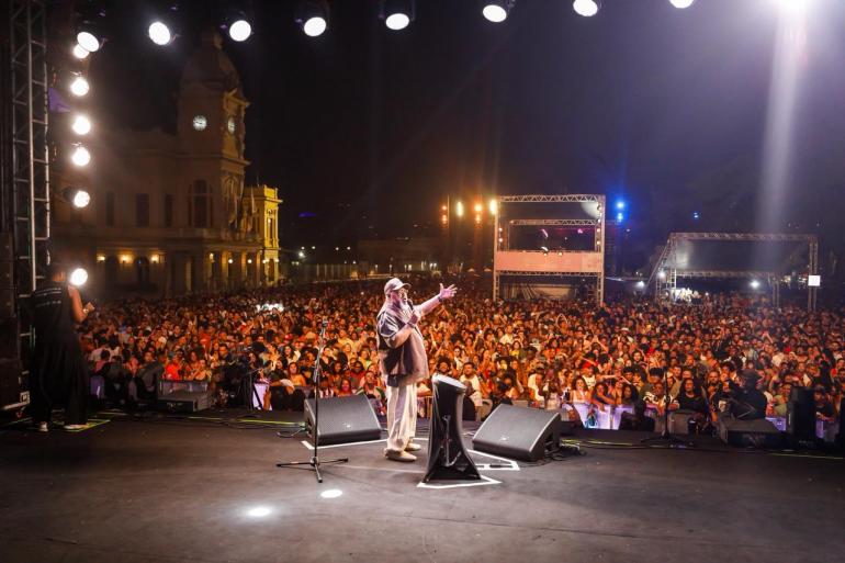 Artista Jorge Aragão em primeiro plano com multidão ao fundo em apresentação na Praça da Estação pela Virada Cultural de 2026