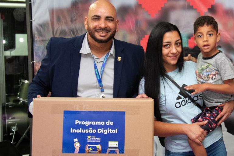 Mutirão da PBH entrega 111 computadores a famílias na Regional Nordeste para promover a inclusão digital Mulher com criança no colo recebe caixa contendo computador de representante da Prodabel