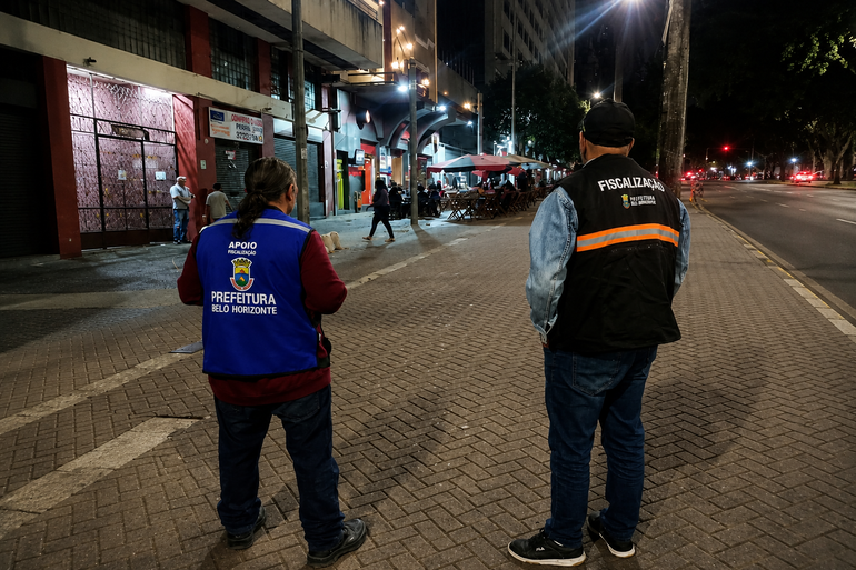Dois homens em é na rua, um vestindo um colete azul e outro com colete preto de Fiscalização da Prefeitura de Belo Horizonte observam a movimentação dos bares na Avenida Amazonas, no Centro de BH.