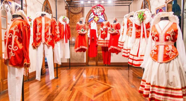Dez trajes folclóricos, masculinos e femininos, nas cores branco e laranja, expostos em sala do Museu de Moda.