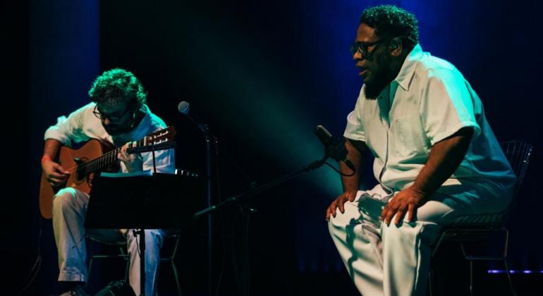 Chico César, Bnegão, Black, Alien, Orkestra Rumpilezz e Mateus Aleluia são alguns dos grandes nomes da música no FAN-BH. Foto: Duda Portella O cantor BNegão ao lado de um homem com violão, ambos sentados, fazendo apresentação musical.