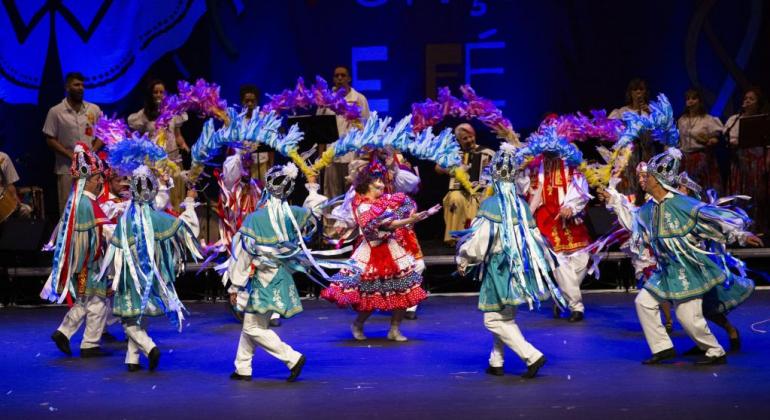 Dez dançarinos, com roupas folclóricas, se apresentam. 