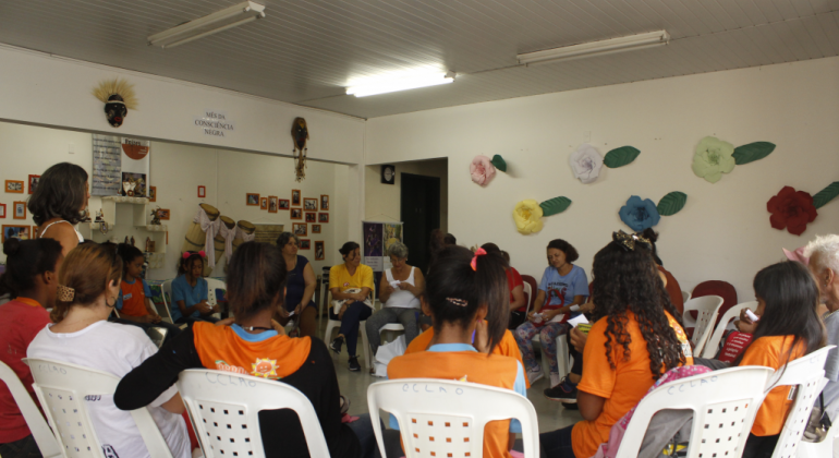 Cinco mulheres, sentadas assistem a Roda de Leitua em centro cultural. 