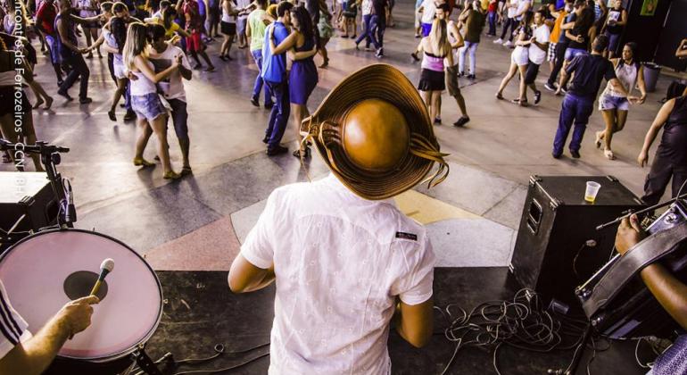 Vista de trás da banda de forró, com vários casais dançando ao fundo. 